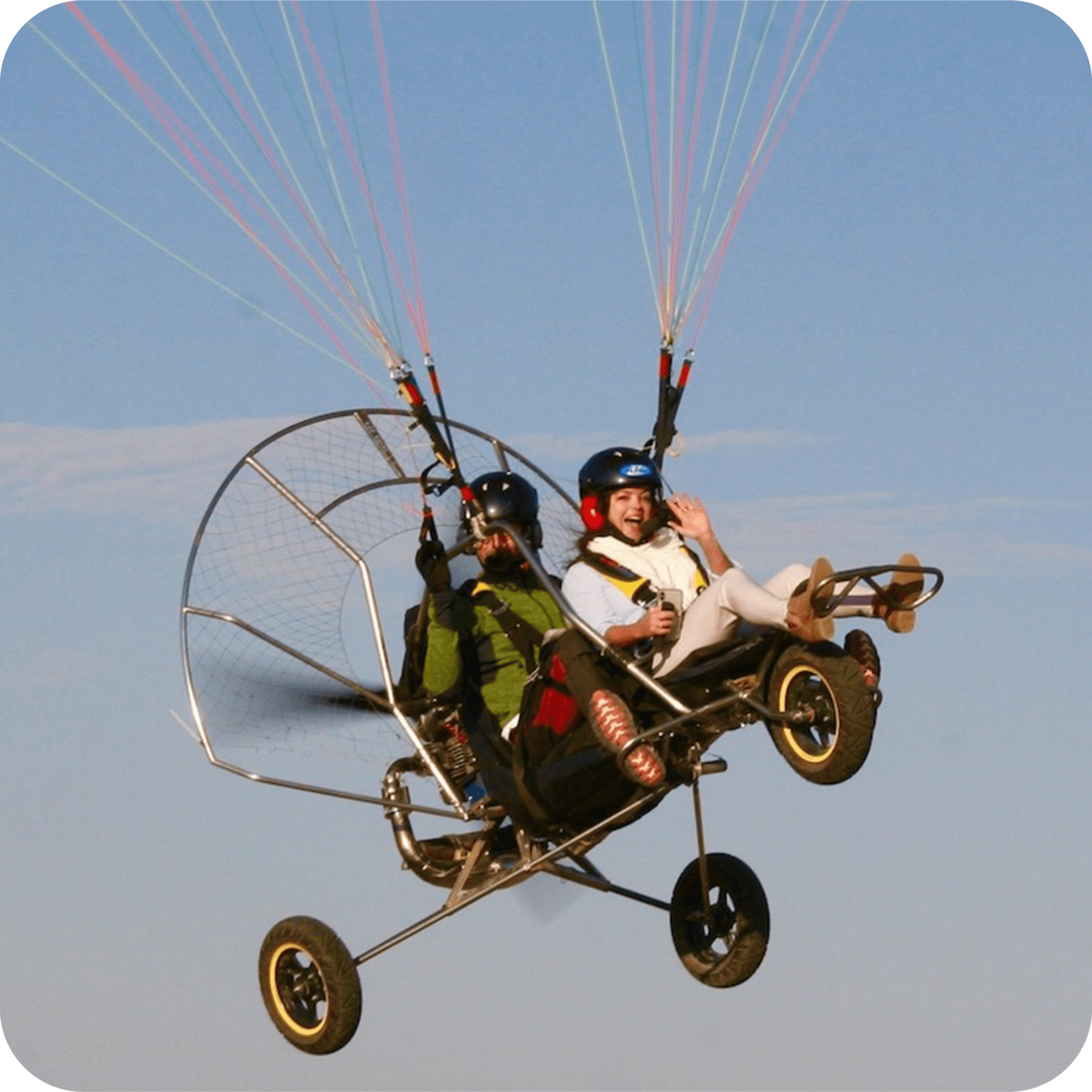 A first-time passenger smiling and waving on a tandem paramotor flight with the instructor.